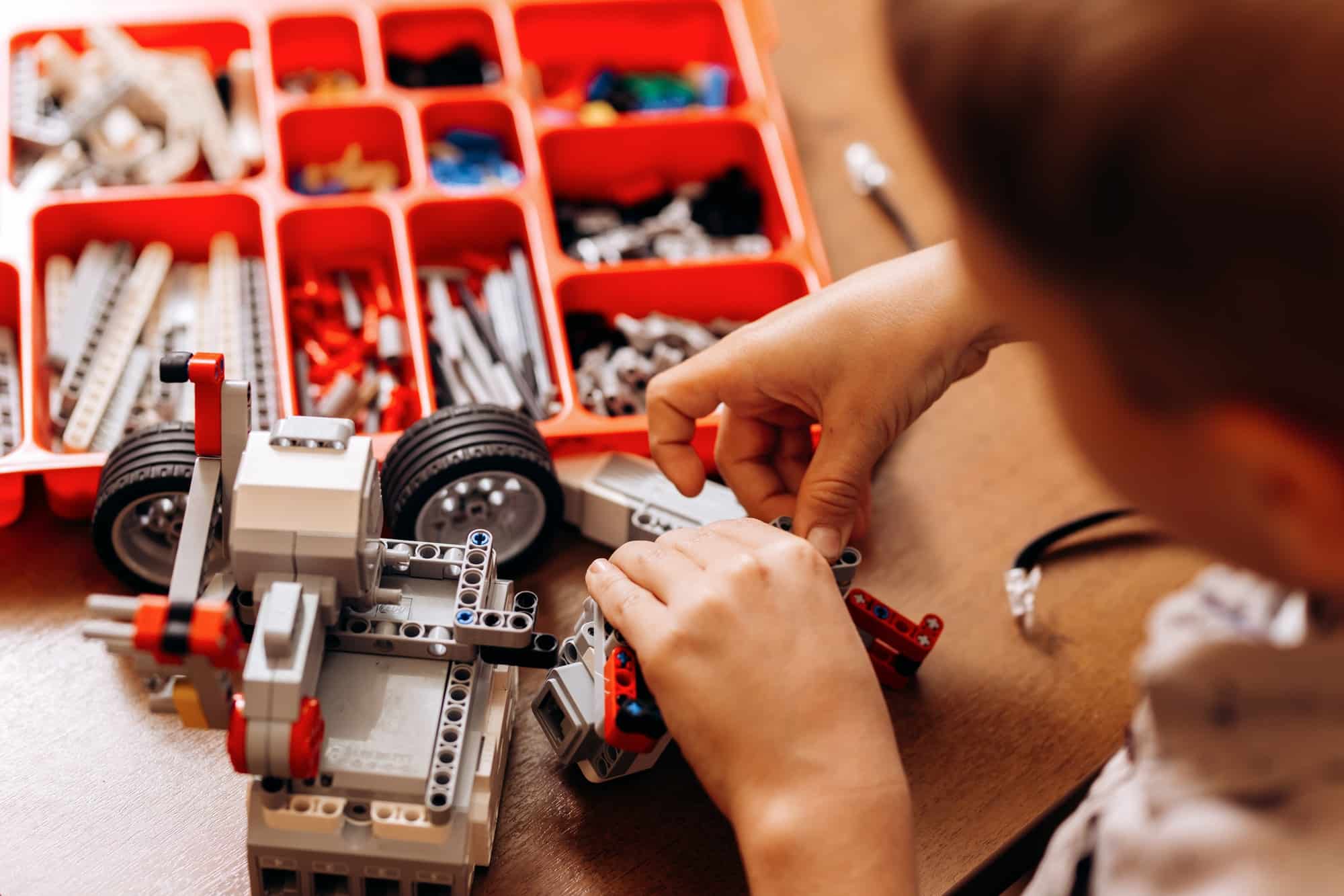 Sedulous boy dressed in gray shirt makes a robot from the robotic constructor at the desk in the