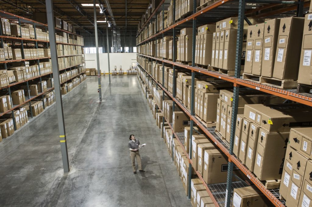 Warehouse worker checking inventory of stock on racks in a distribution warehouse.