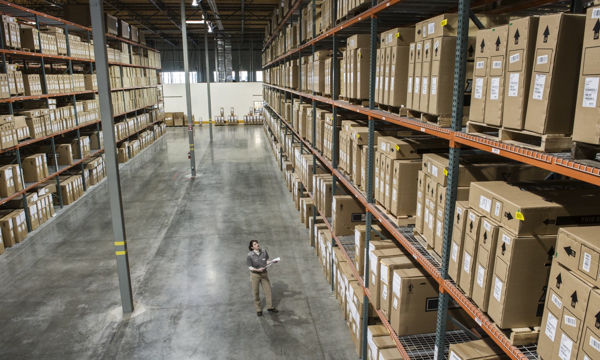 Warehouse worker checking inventory of stock on racks in a distribution warehouse.